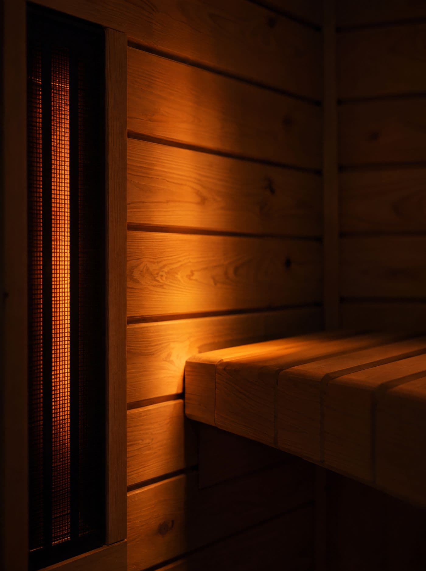 Intérieur d'un sauna infrarouge : lames d'épicéa et banc baignés d'une lumière ambrée